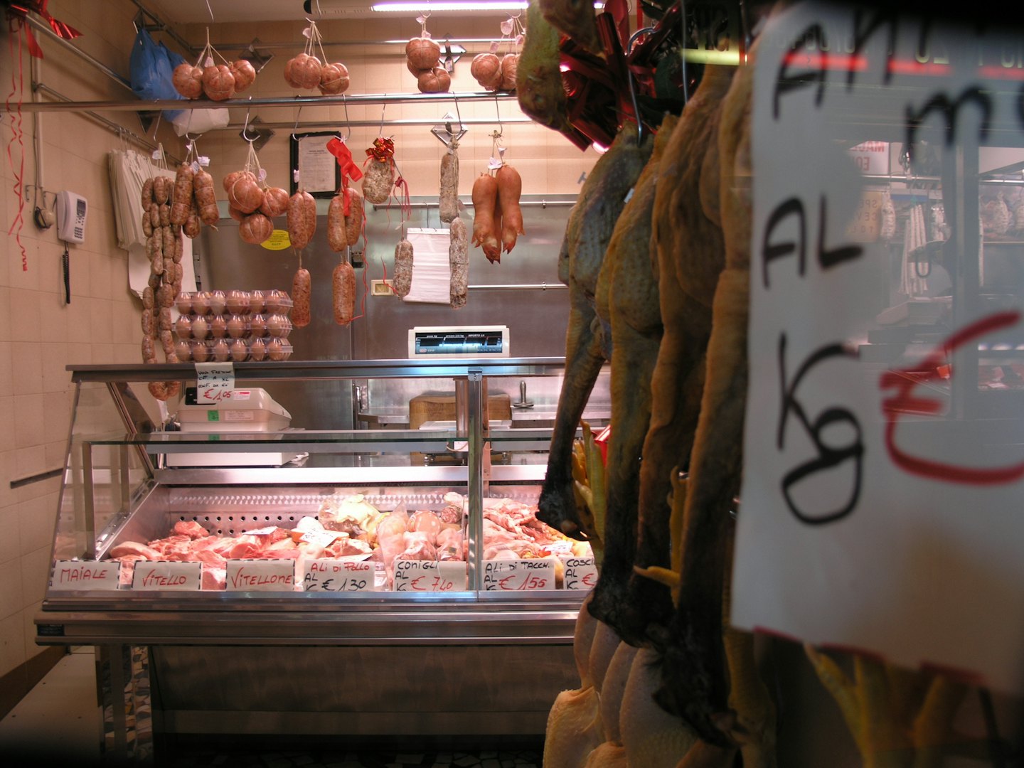 Carne cruda e salsicce appese all'interno di una vetrina di macelleria.