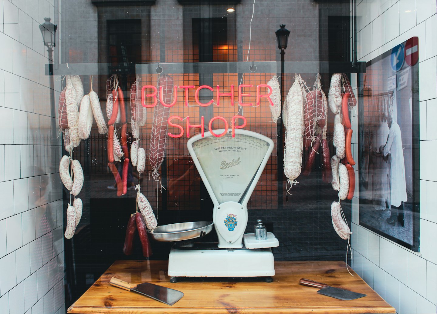 Vetrina di una macelleria con carni appese e un'insegna al neon.