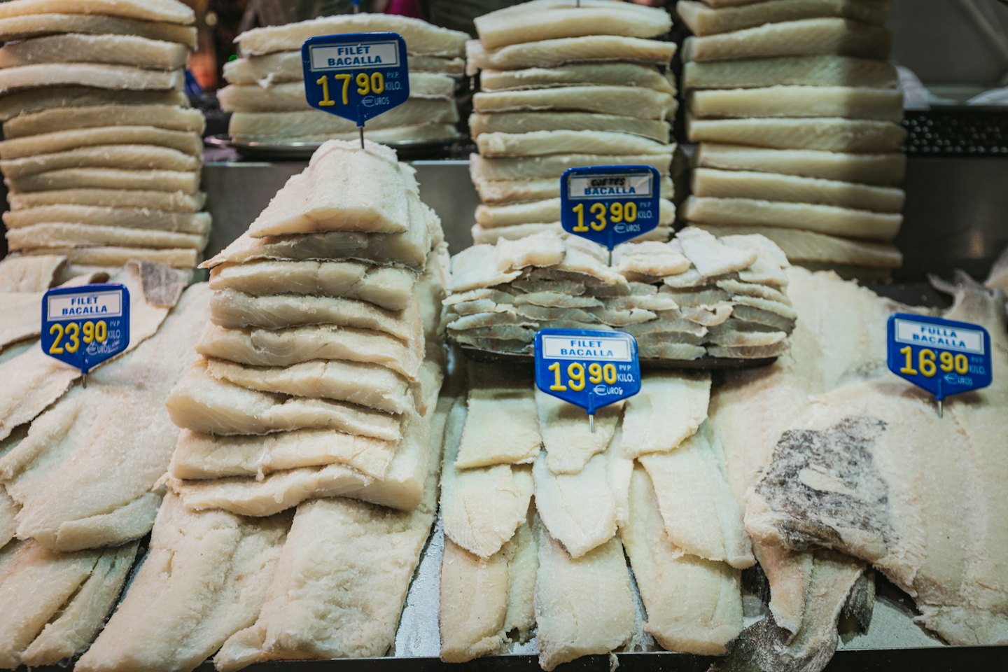 Pile di merluzzo salato con cartellini dei prezzi in un mercato.